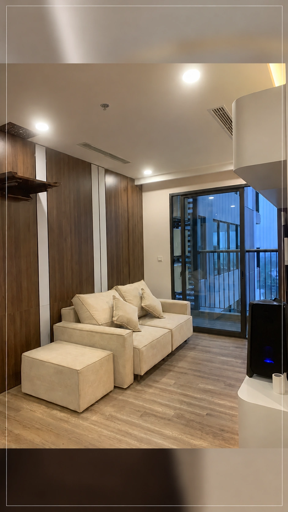 Sofa hai chỗ và đôn rời đặt bên vách vân gỗ gần ban công