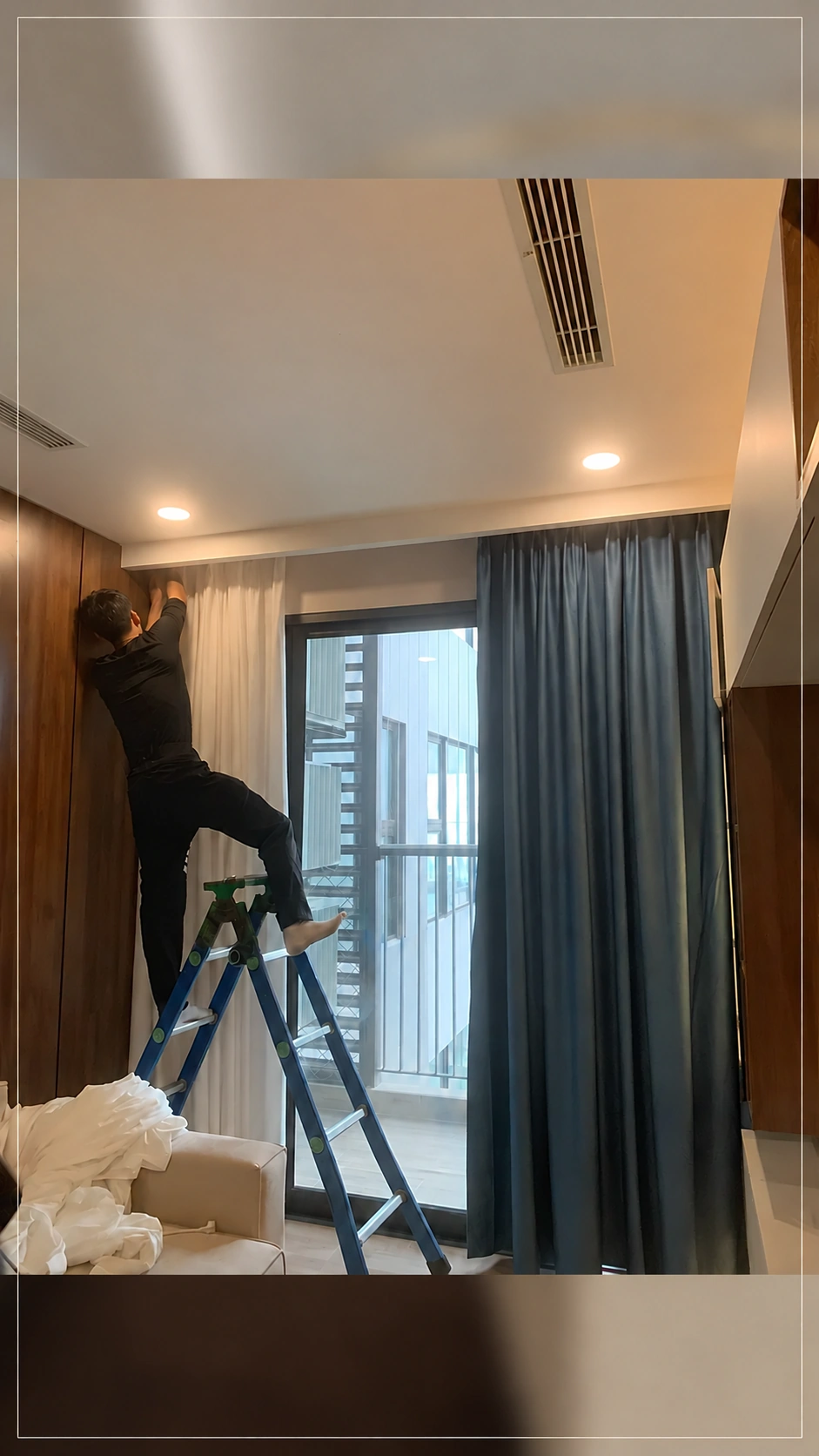 Thợ lắp lớp voan trắng và rèm vải xanh tại cửa kính phòng khách