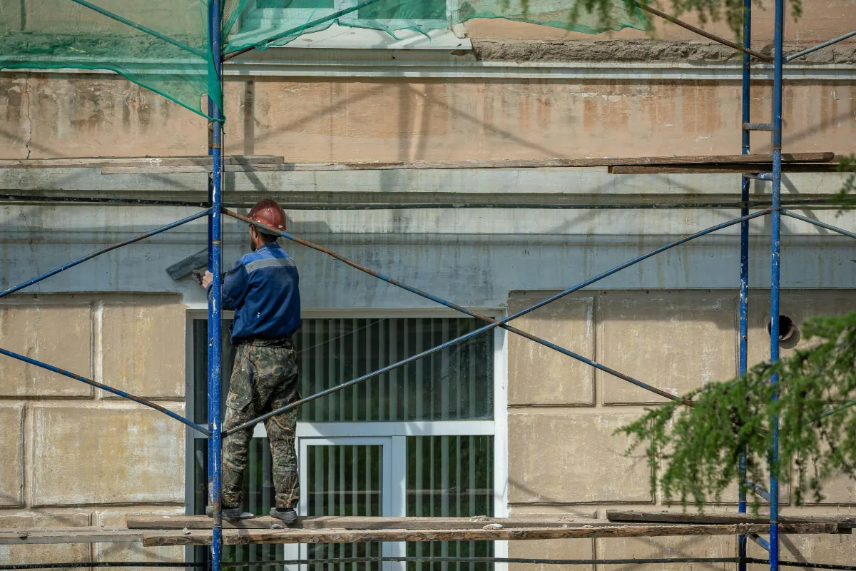 Thợ làm việc trên giàn giáo để sửa lớp hoàn thiện mặt ngoài nhà