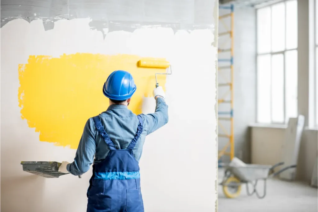 Người thợ đội mũ bảo hộ dùng con lăn sơn màu vàng lên tường