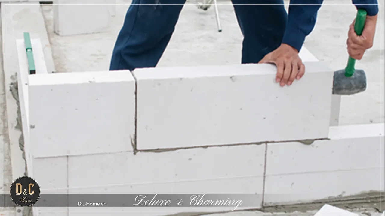 Thợ chỉnh vị trí viên gạch màu sáng trên hàng tường bằng dụng cụ cầm tay